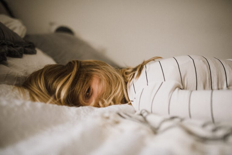 Picture of a woman laying in bed, experiencing the symptoms of burnout